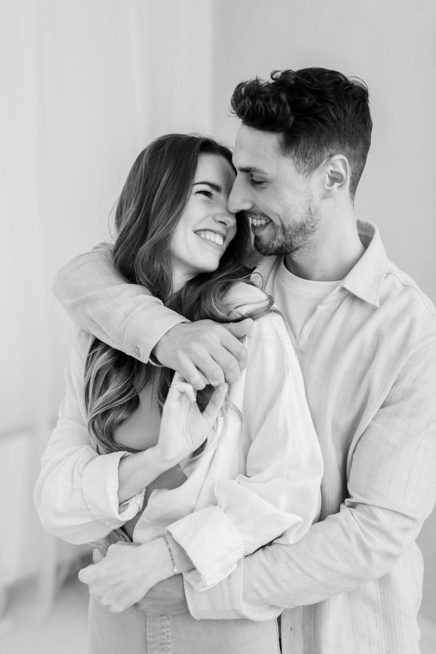 Black and white portrait of a couple embracing and laughing together against a light background.