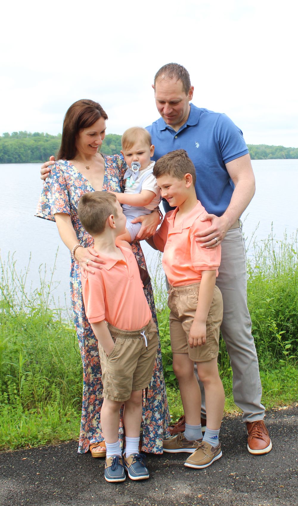 A family of five shares a tender moment together by a scenic lake.