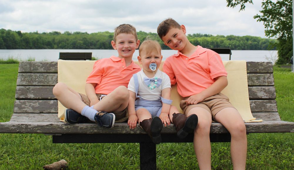 Three individuals sit together on a park bench by a lake.