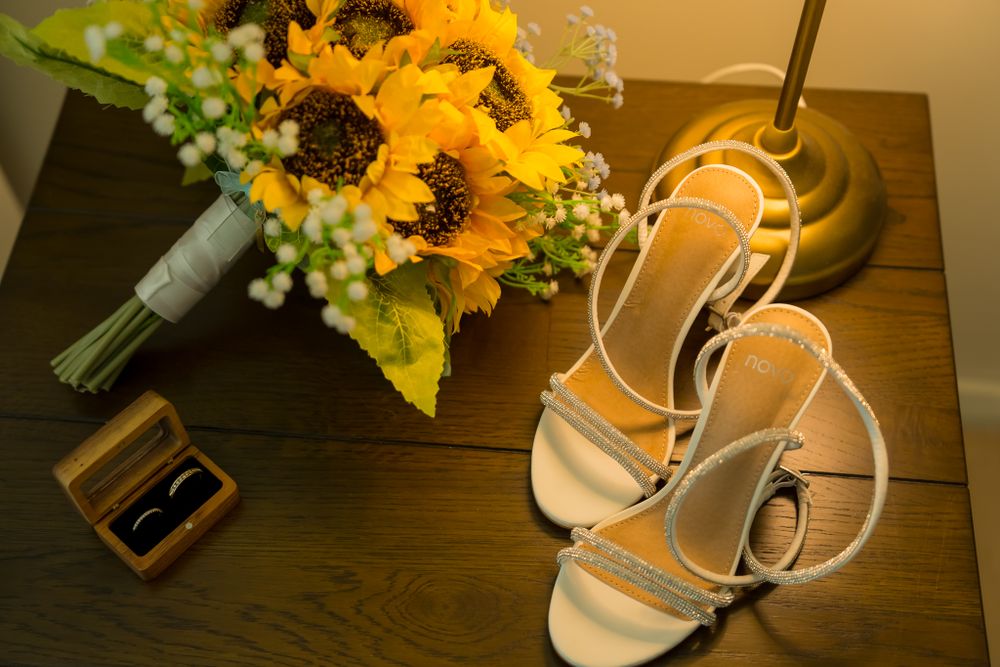 Wedding accessories including sunflowers and white sandals arranged on wooden surface.
