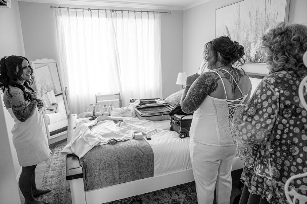 A wedding preparation scene in a bright hotel room with a white dress being fitted.