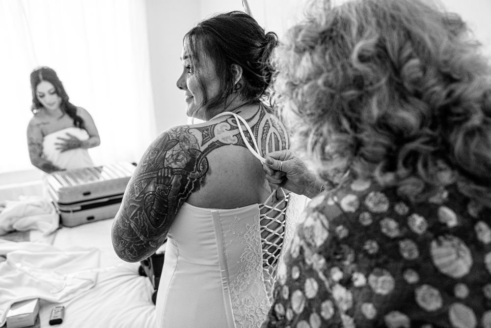 Back view of a detailed corset-style wedding dress being laced up in a bright room.