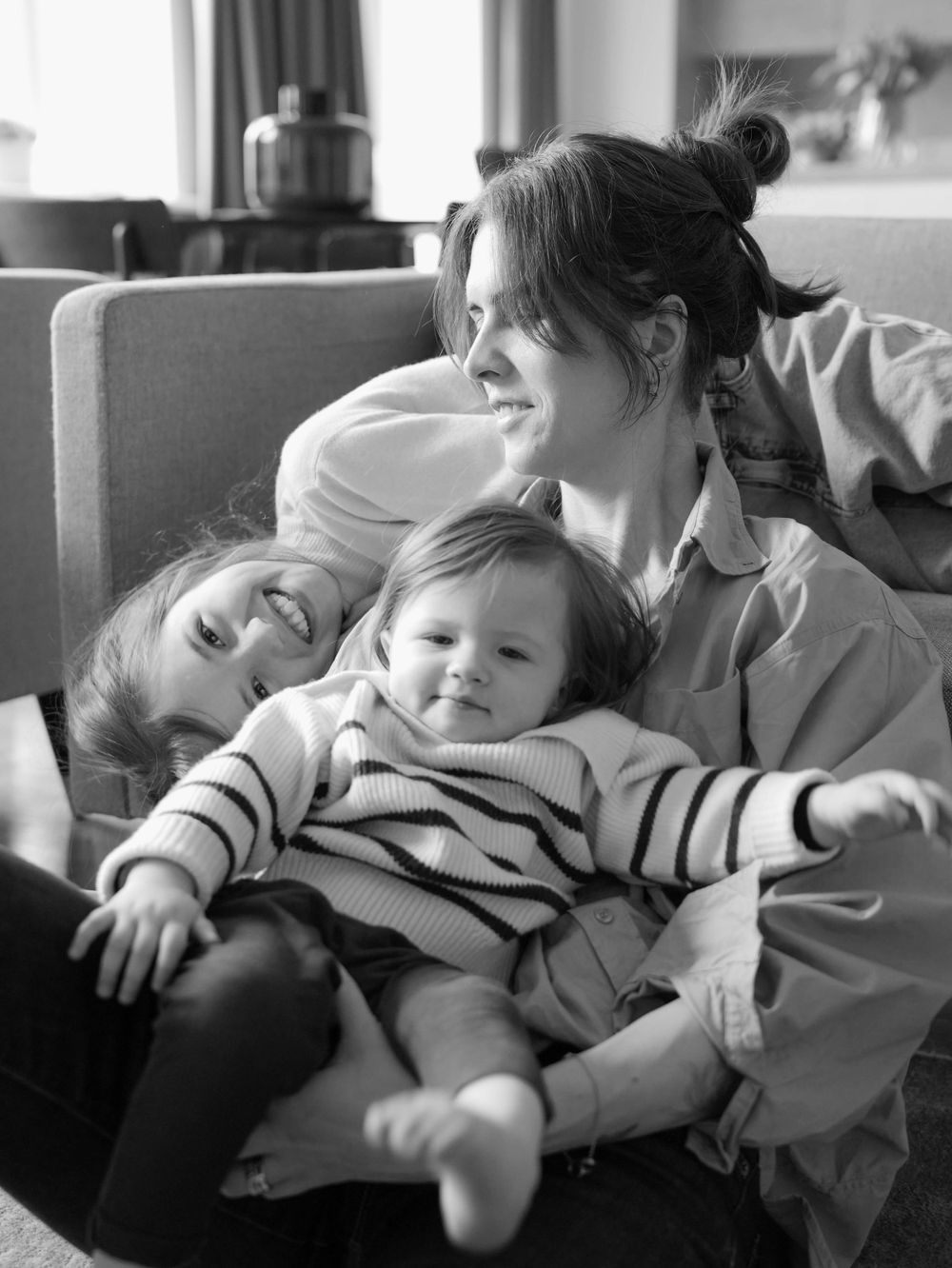 Mother and two small daughters sit on the ground.