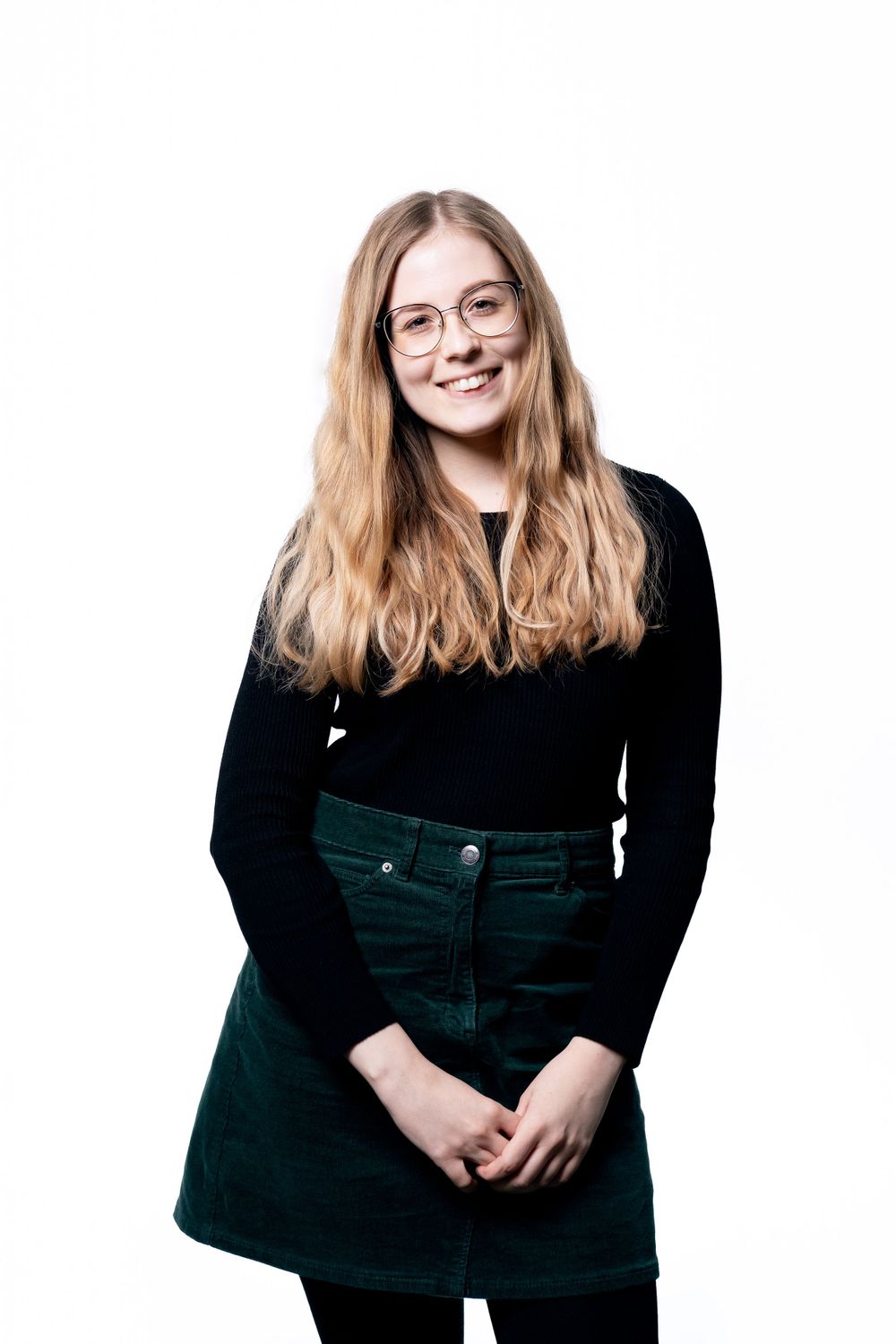 Studio shot of person wearing black sweater and green corduroy skirt against white background.