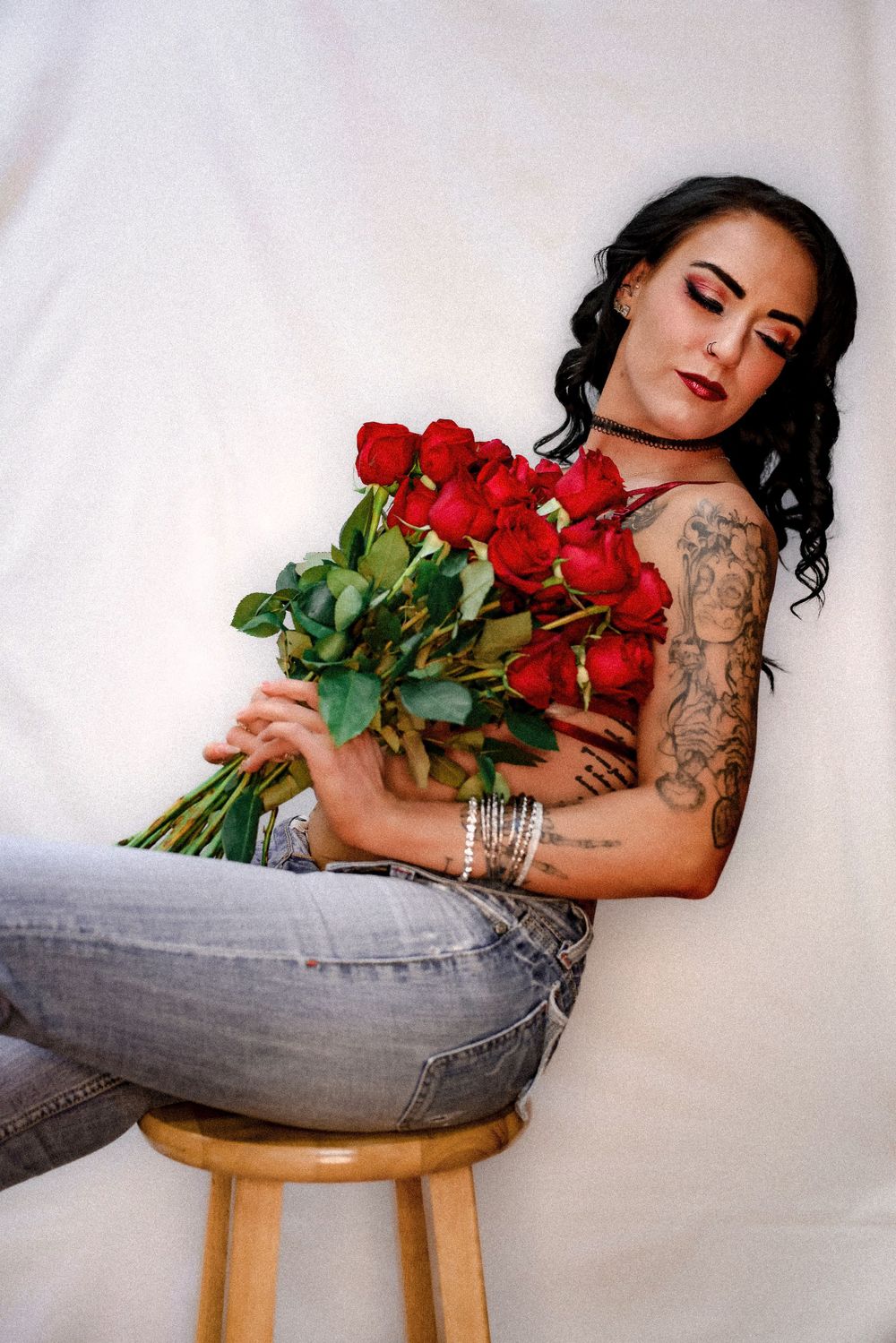 Artistic portrait with red roses bouquet and tattoos in casual denim.