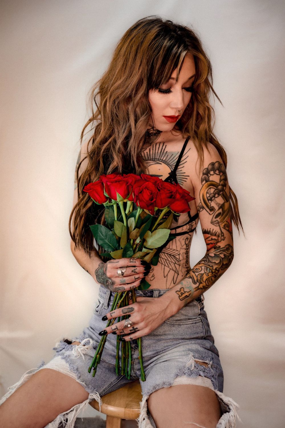 Moody portrait with red roses and tattoo sleeve wearing distressed denim shorts.