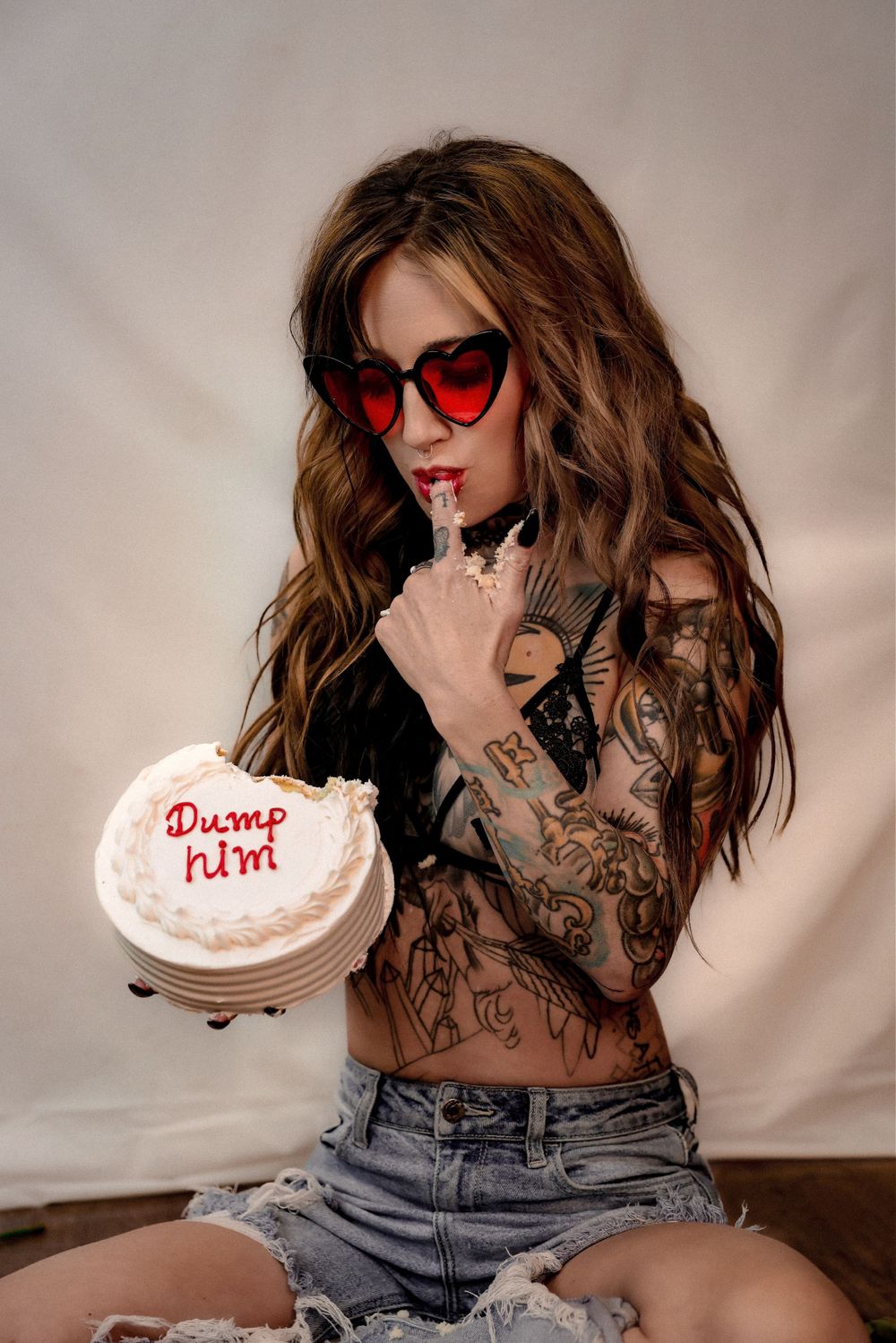 Fashion portrait with heart-shaped red sunglasses and white cake with text.