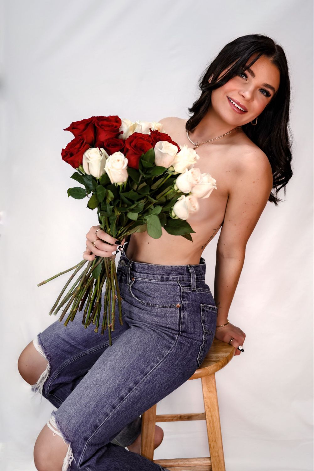 Artistic photo with red and white roses held by someone wearing ripped jeans and sitting on a wooden stool.