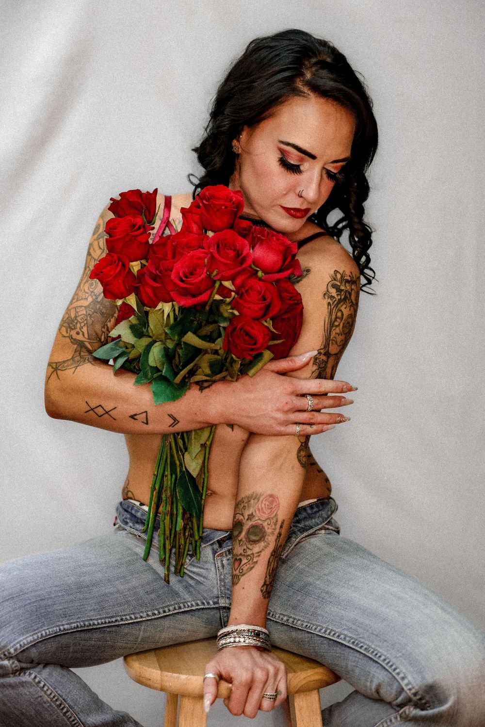 Intimate portrait embracing red roses bouquet while sitting on wooden stool.