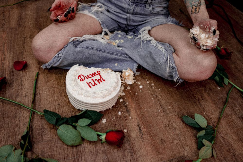 Overhead shot of cake and scattered rose petals on wooden floor.