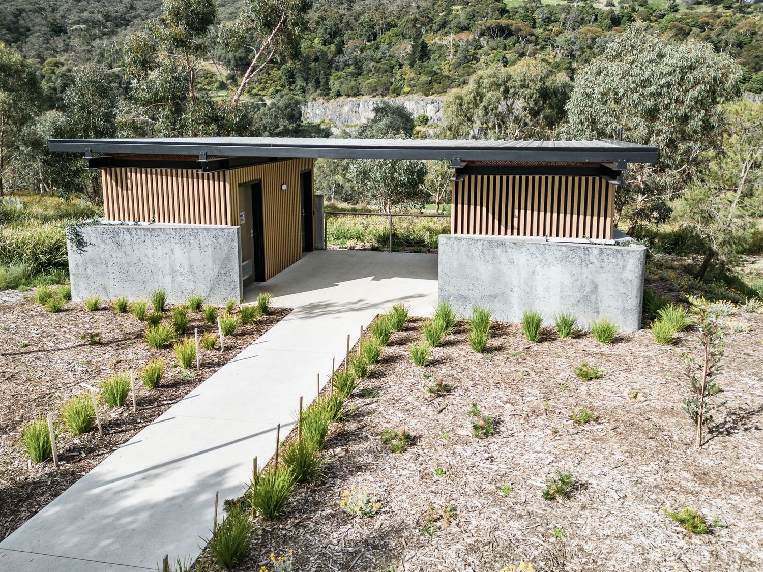 Symmetrical outdoor pavilion with concrete base and wooden screens connected by central walkway.
