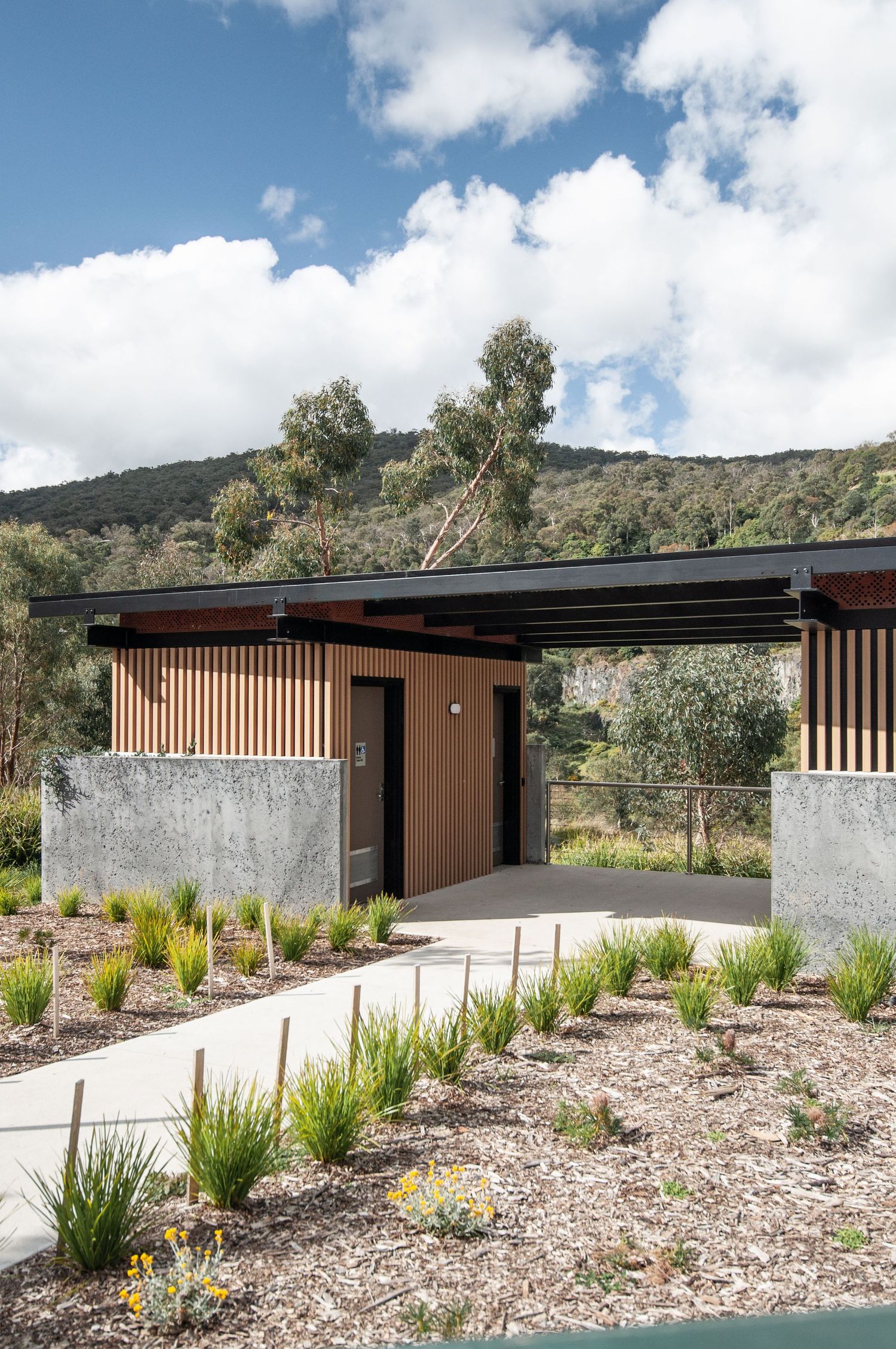 Modern outdoor structure with wooden slats and concrete walls set against a mountainous landscape.