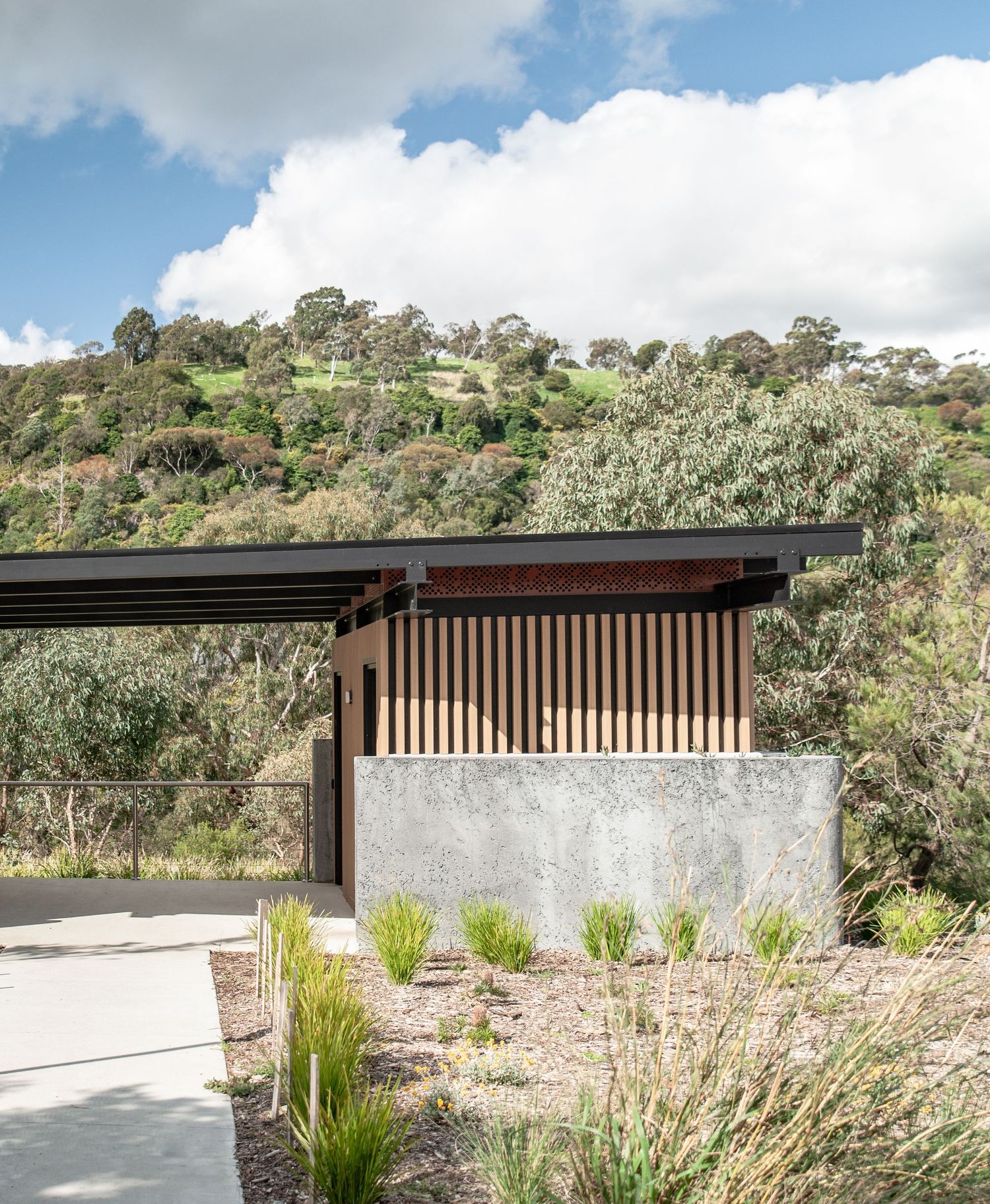 Minimalist outdoor structure with wooden screens and concrete base nestled in hillside setting.
