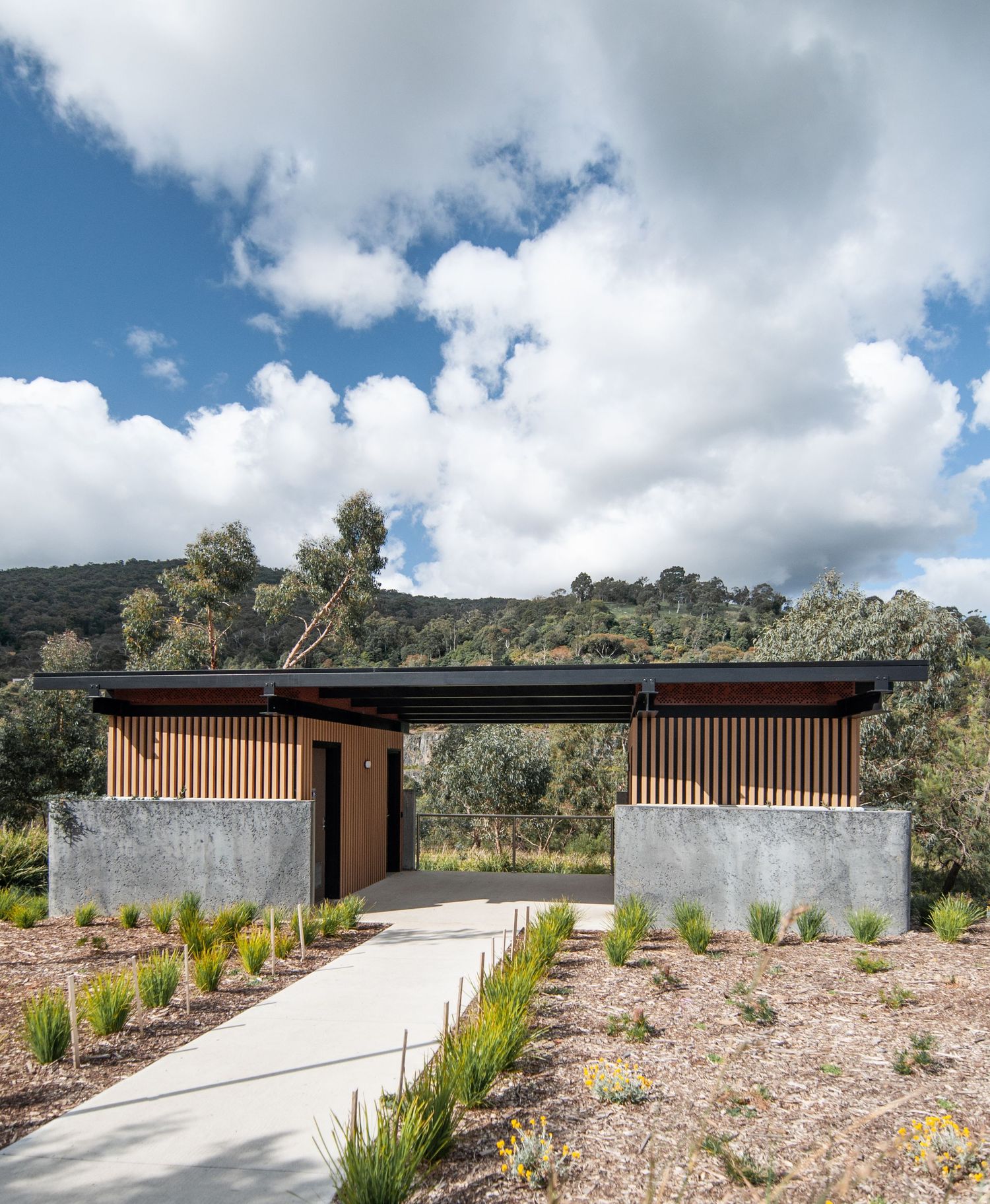 Contemporary outdoor structure with wooden screens and concrete walls set against blue mountain sky.