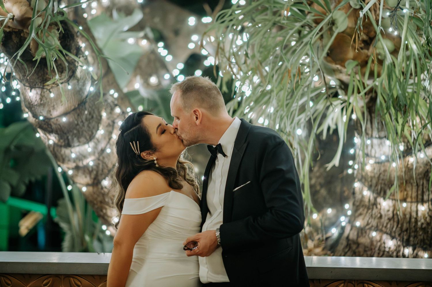 Romantic moment under twinkling lights and greenery at an evening wedding reception.