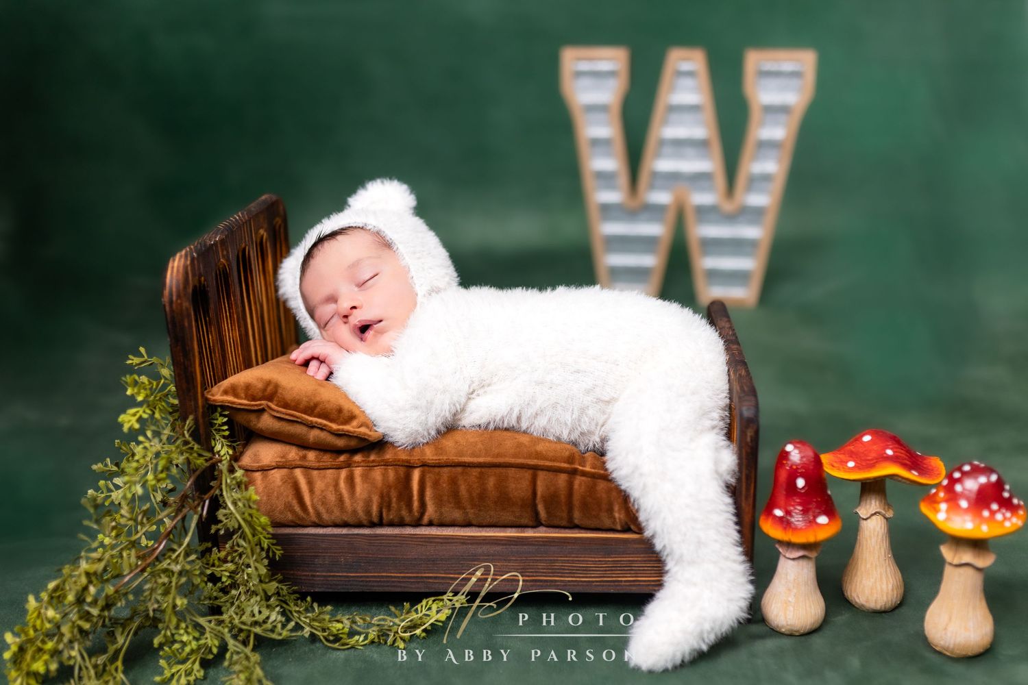 A sleeping figure dressed in a white fluffy costume lies on a brown leather couch with decorative mushrooms and greenery nearby.