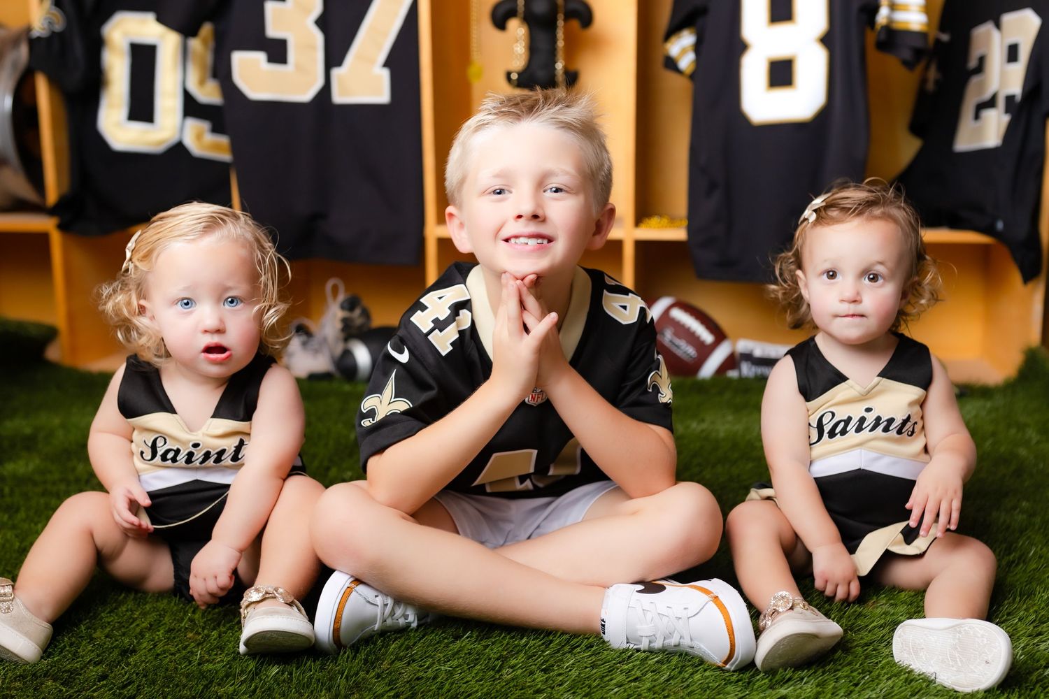 Young athletes sit together on locker room floor with sports jerseys displayed in background.