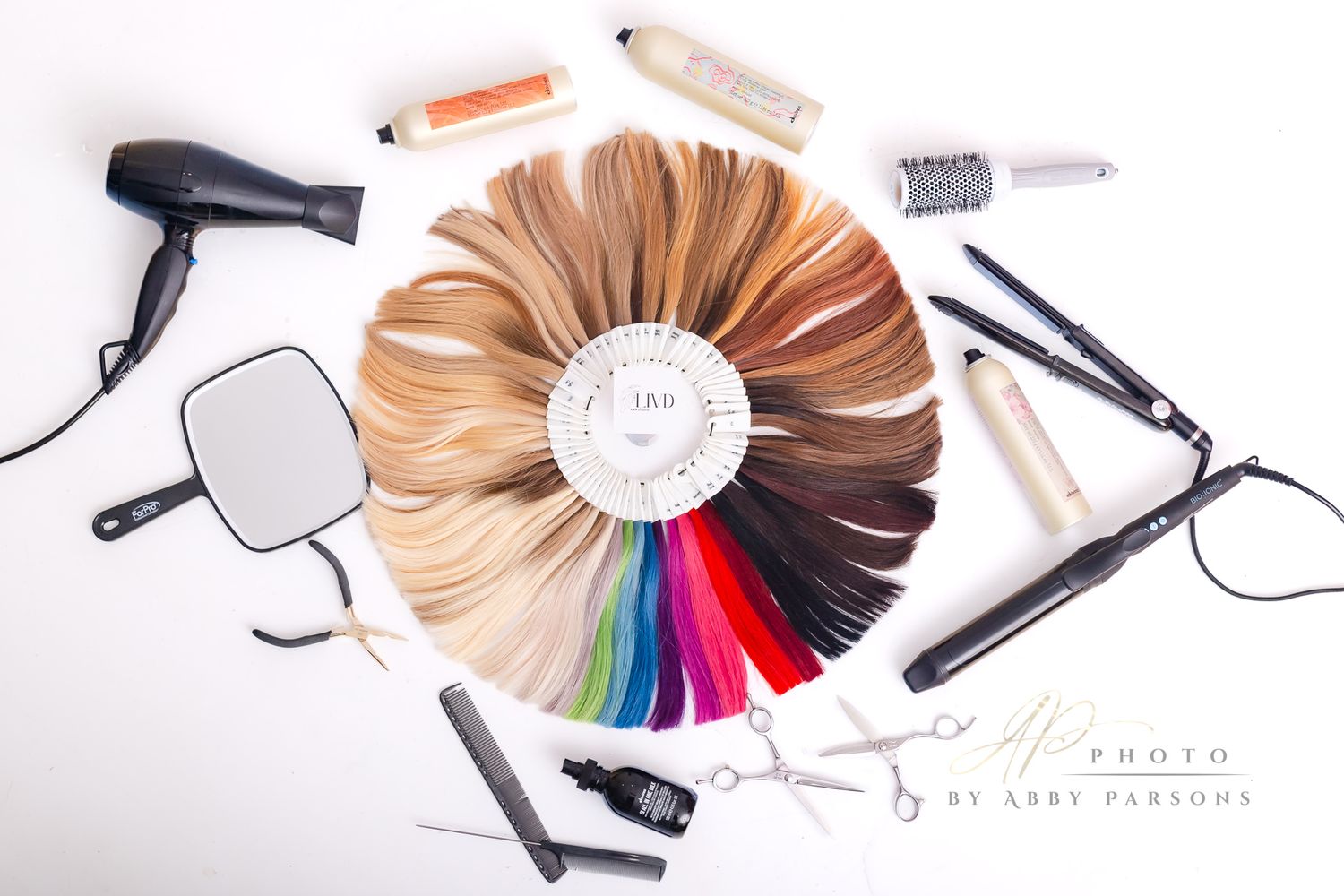 Hair color swatch wheel with styling tools including hairdryer, flat iron and accessories arranged on white background.