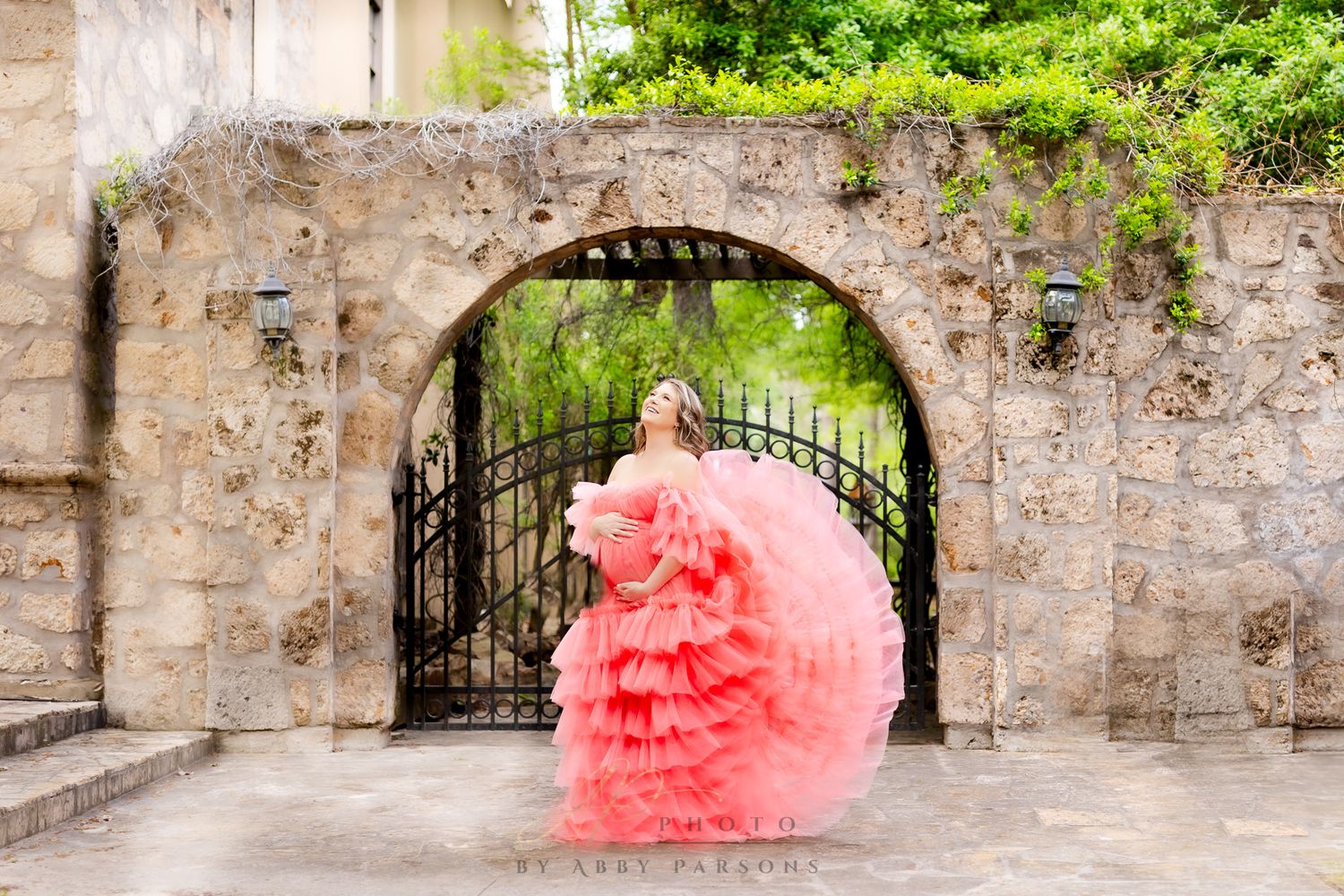 Flowing coral pink ballgown dress photographed in front of a stone archway and iron gate.