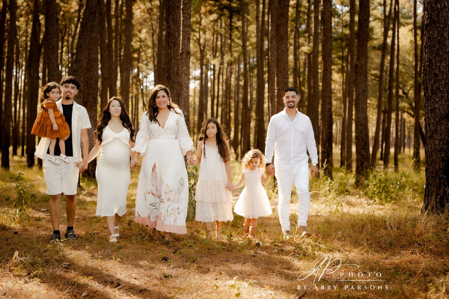 A group in white clothing walks together through a sunlit forest path during golden hour on a summer evening.