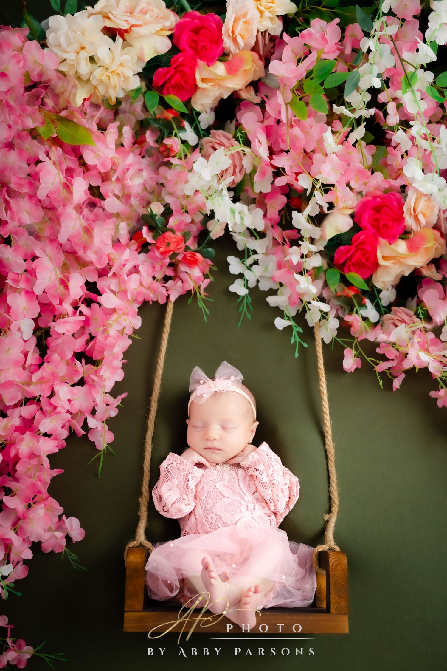 Wooden swing adorned with pink and peach floral decorations against a dark background creates a dreamy spring scene.