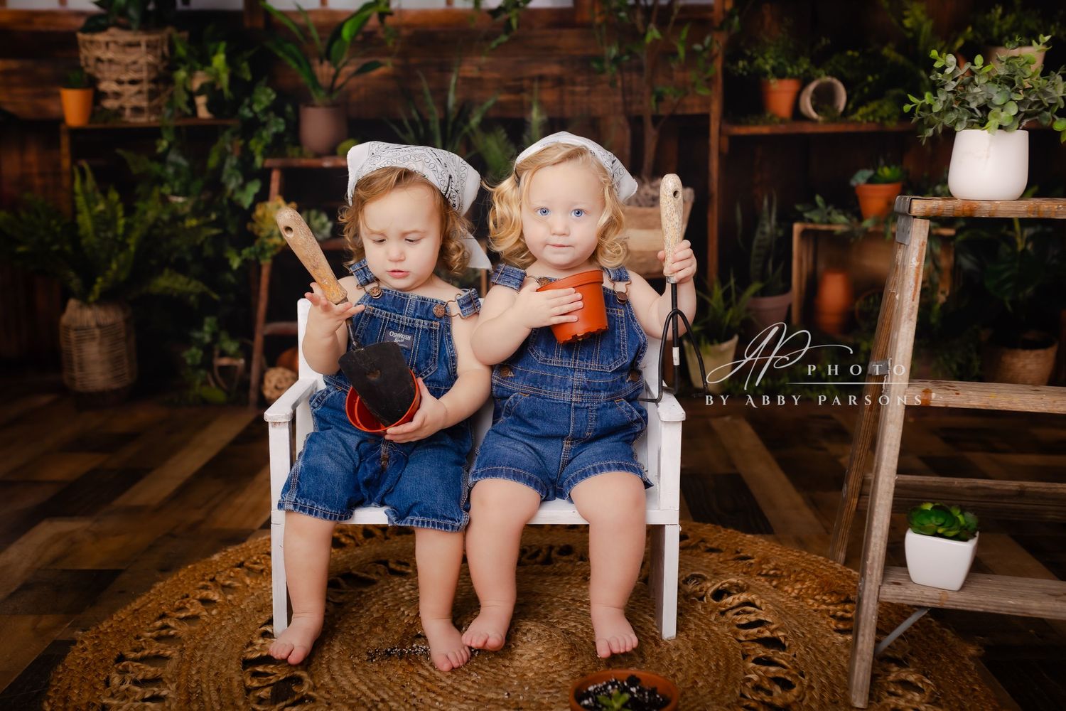 Two young children in denim overalls sit on a white bench while holding milk bottles in a cozy rustic setting.