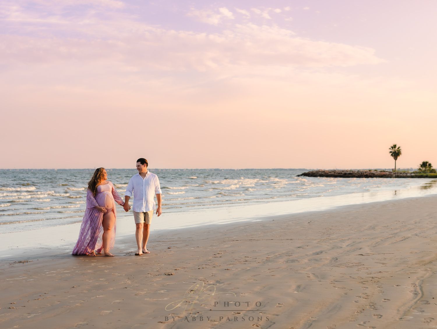 Couple walking together on a sandy beach at sunset with ocean waves in the background.