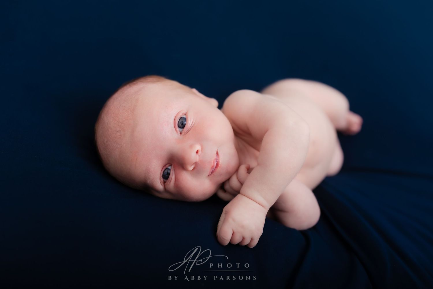 A newborn baby lying on a dark blue blanket during a professional studio photography session.
