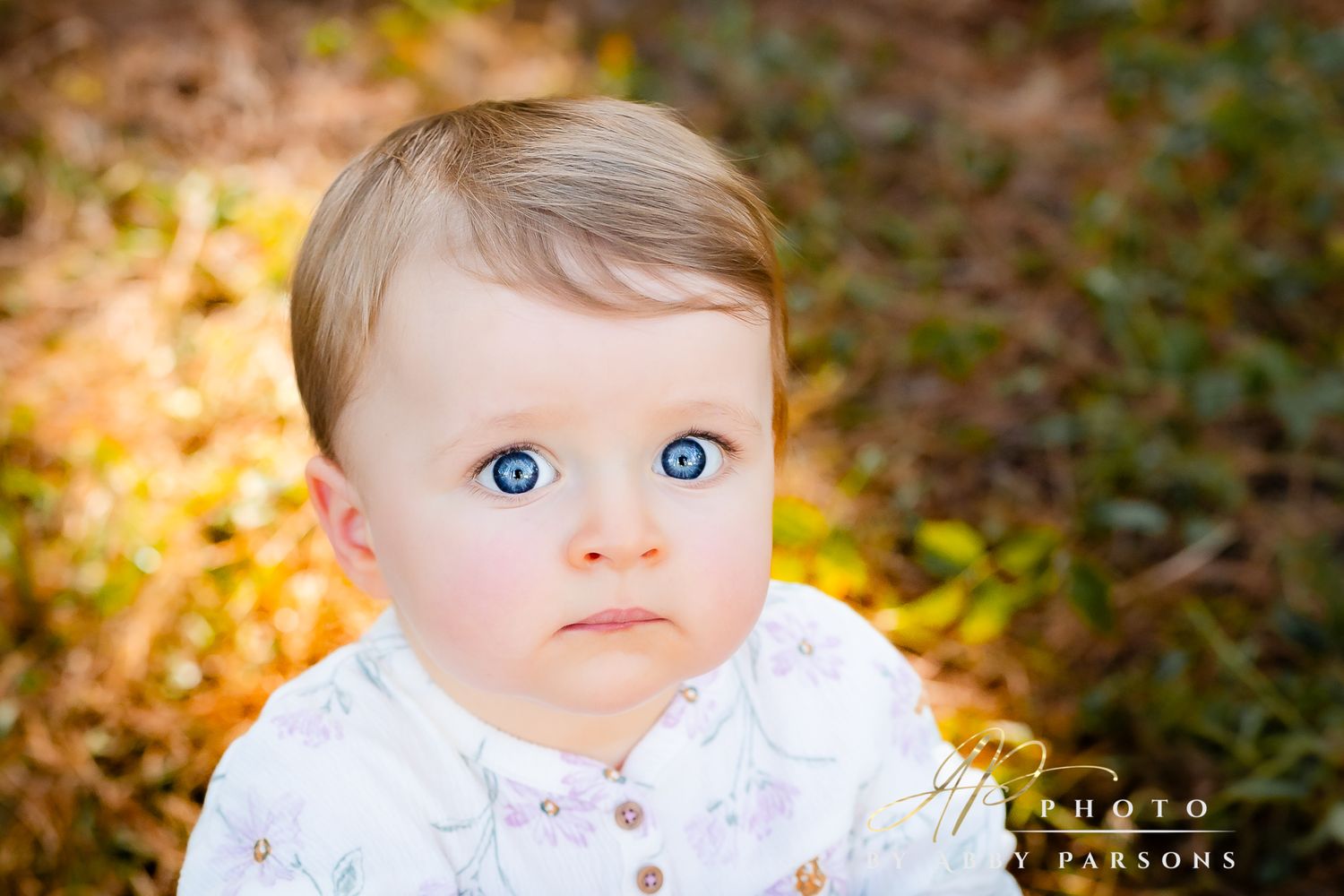 Close up outdoor portrait of a young child in white clothing with striking blue eyes against a soft blurred background.