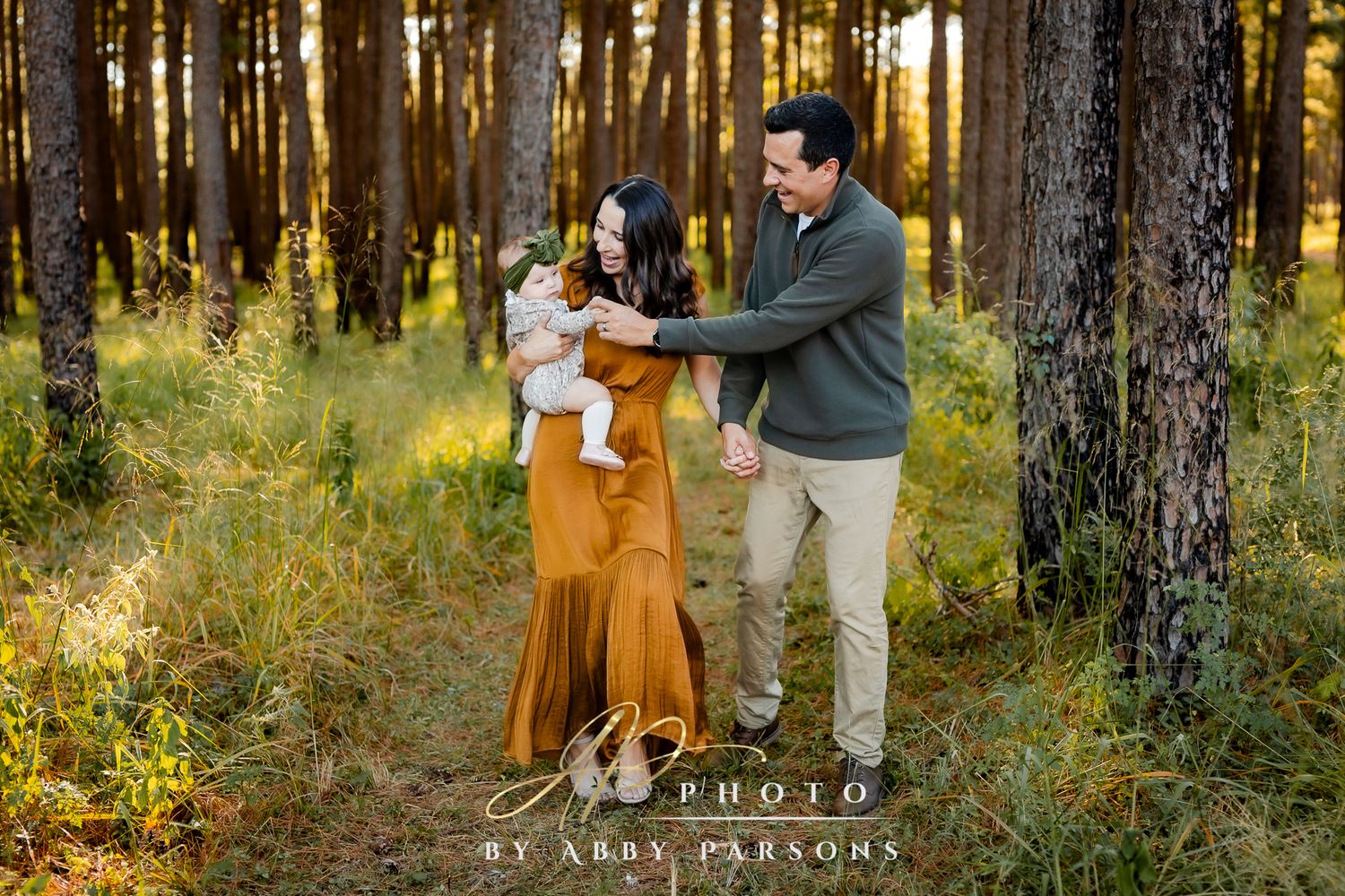 Family shares a sweet moment together in a sunlit pine forest with golden evening light filtering through the trees.