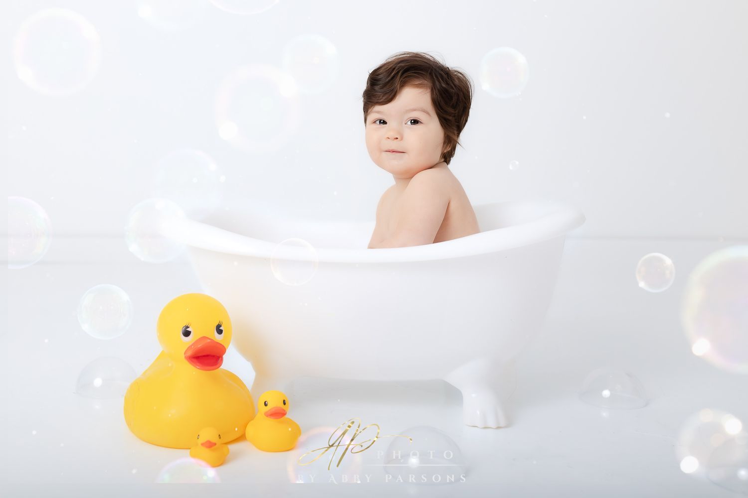 Bath scene with white clawfoot tub, floating bubbles, and yellow rubber ducks on a light gray background.