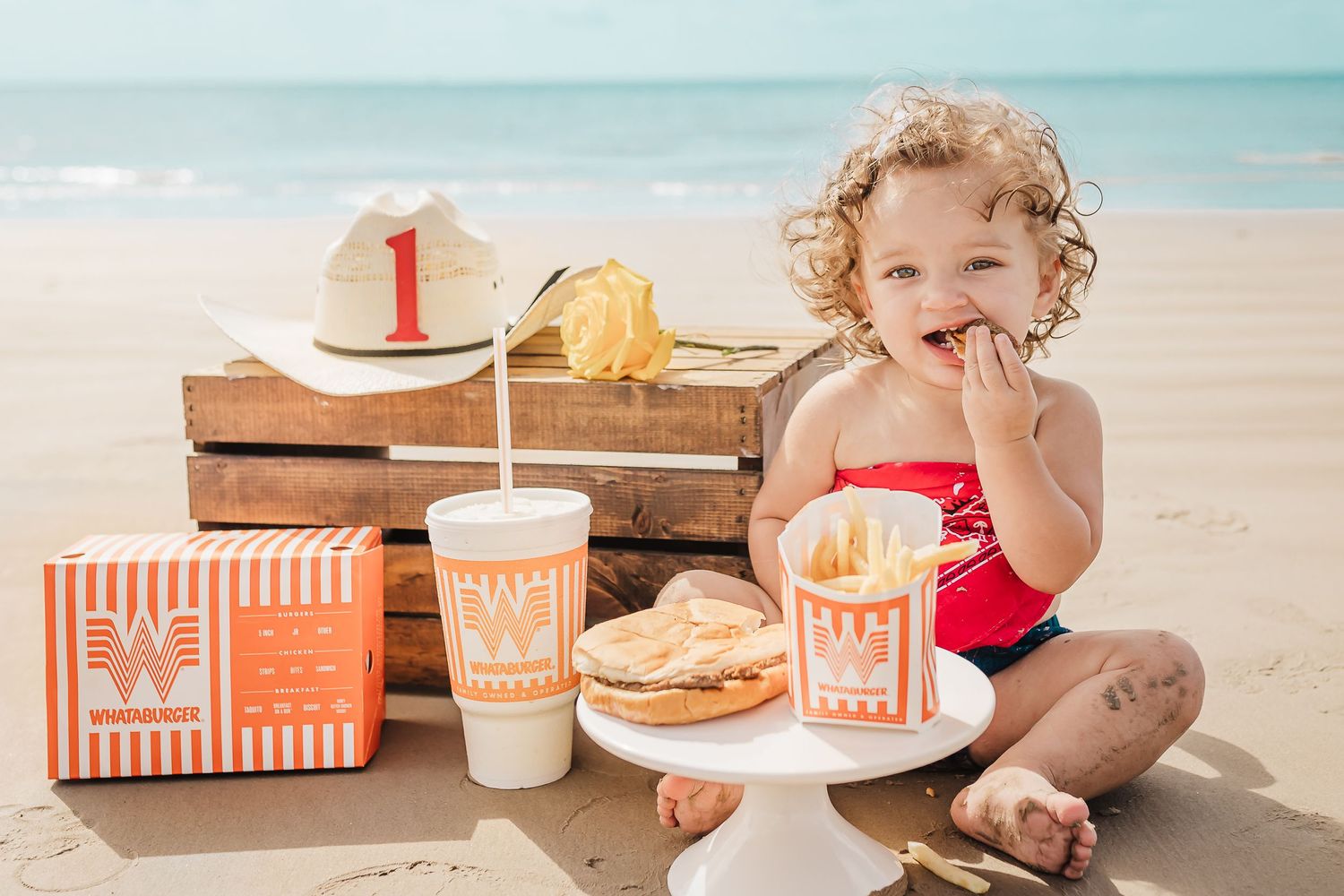 A beach picnic setup with Whataburger fast food including fries, burgers and drinks on a sunny day by the ocean.
