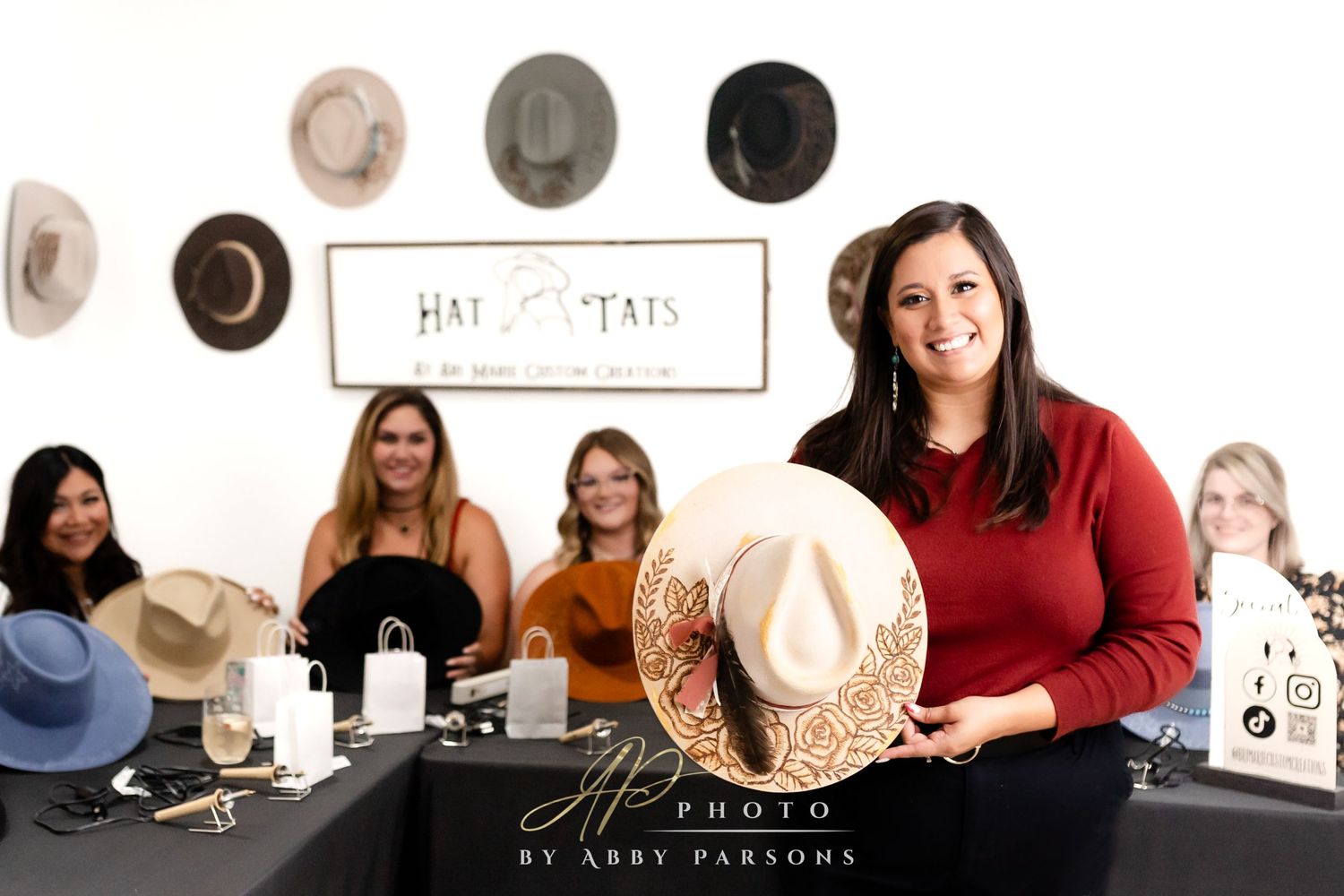 Group of friends gather around a table displaying hat merchandise for a small business.