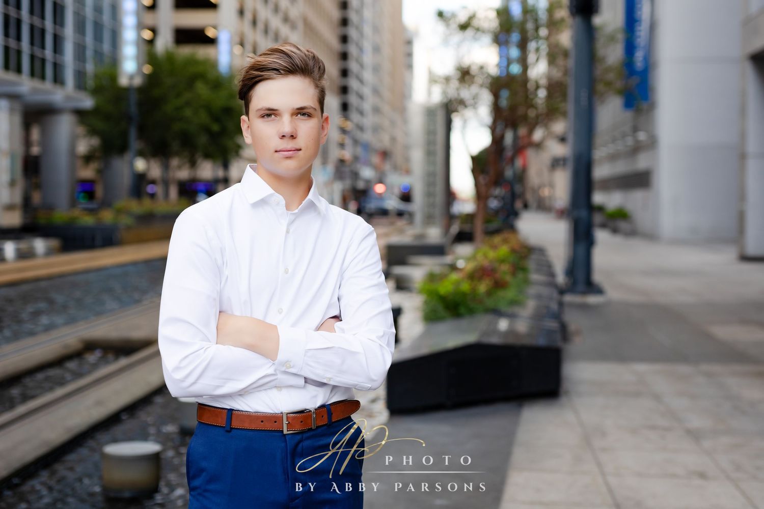 Professional portrait against an urban backdrop with modern buildings and railway tracks visible.