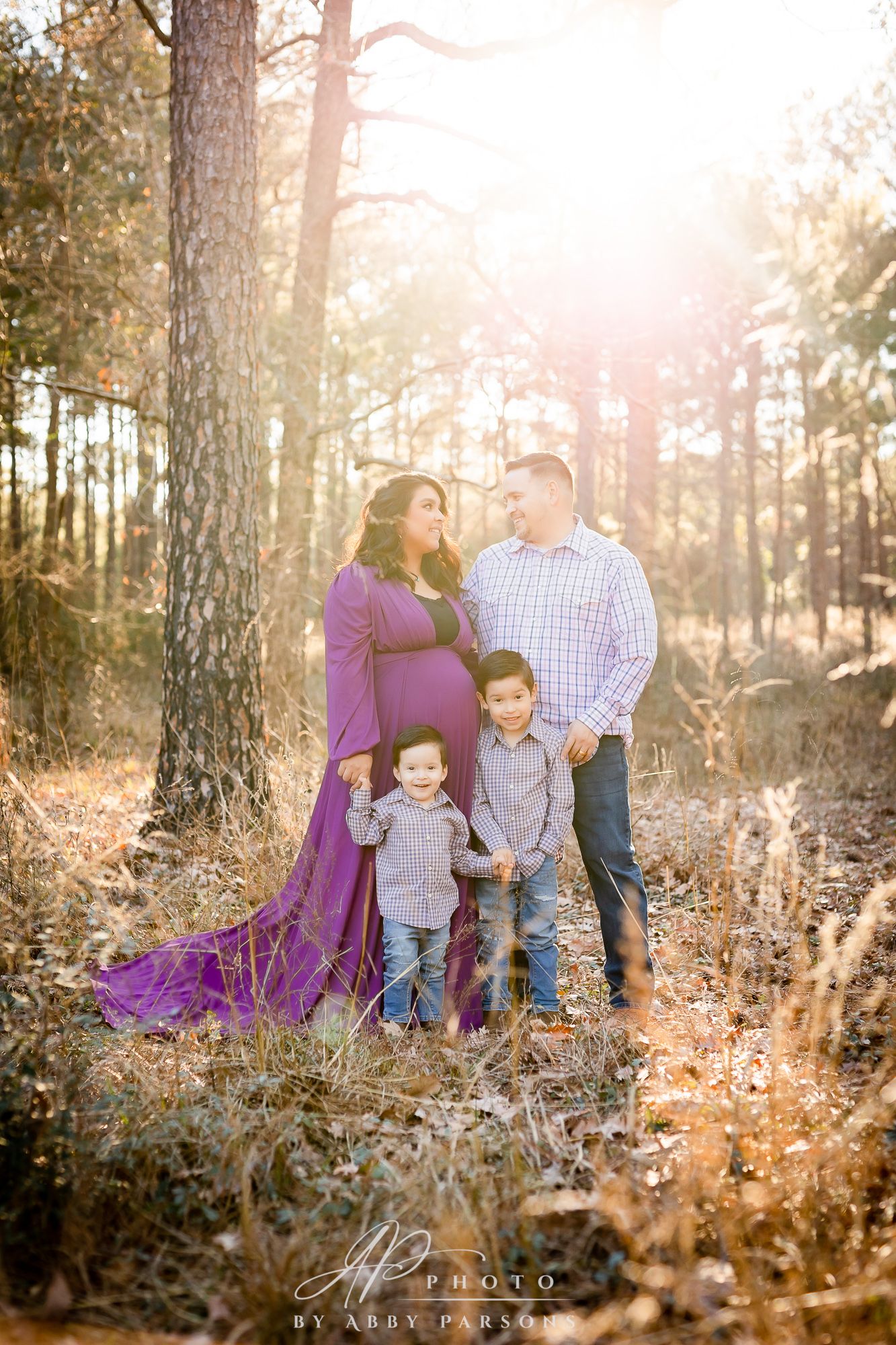 Beautiful fall family maternity photo in a sunlit forest with backlit golden light and glowing sunset ambiance.