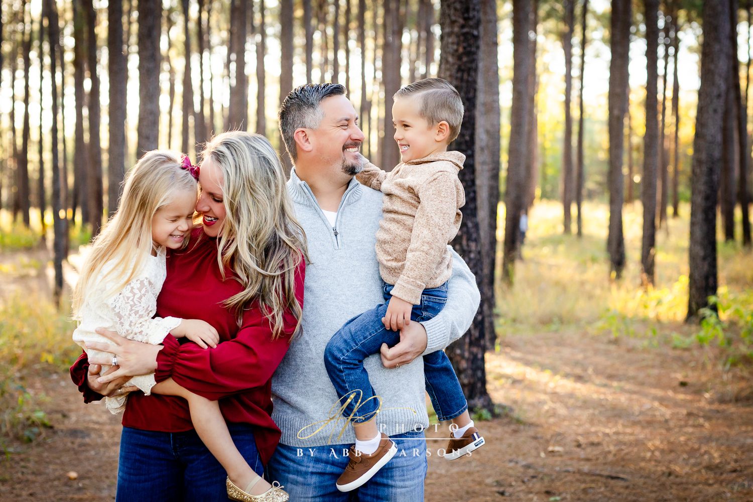 Family of four laughs together while enjoying an afternoon in a sunlit pine forest.