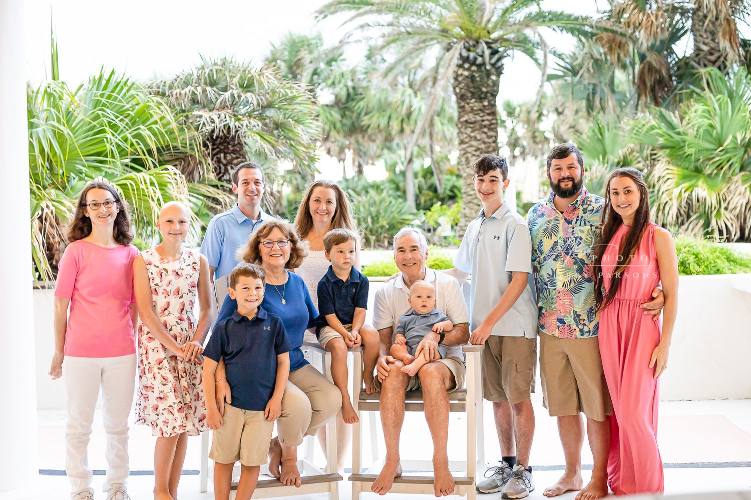 A group poses together outdoors against a backdrop of tropical palm trees on a sunny day.
