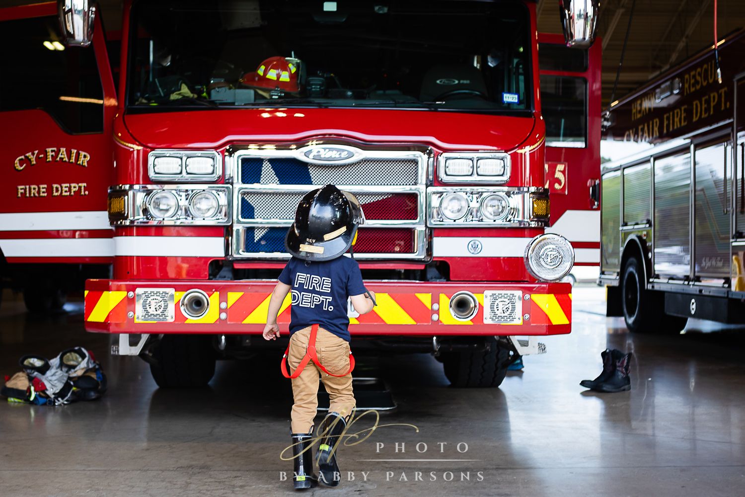 Small child in blue shirt and shorts exploring a bright red fire truck inside a fire station.