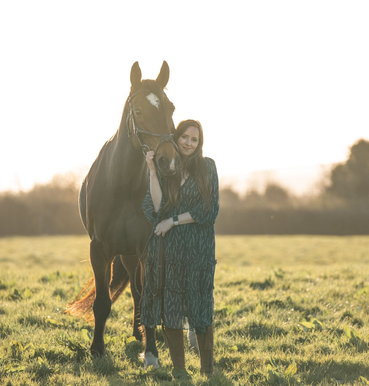 A dark horse stands with handler in plaid shirt at sunset by a wooden fence.