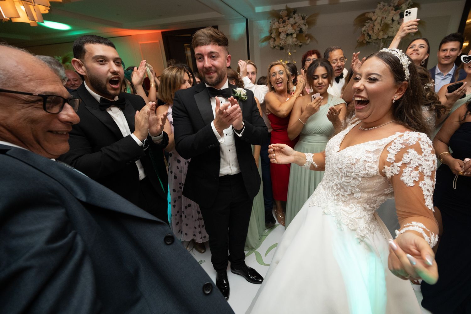 Wedding guests celebrate and dance with excited bride on lively dance floor at wedding reception.