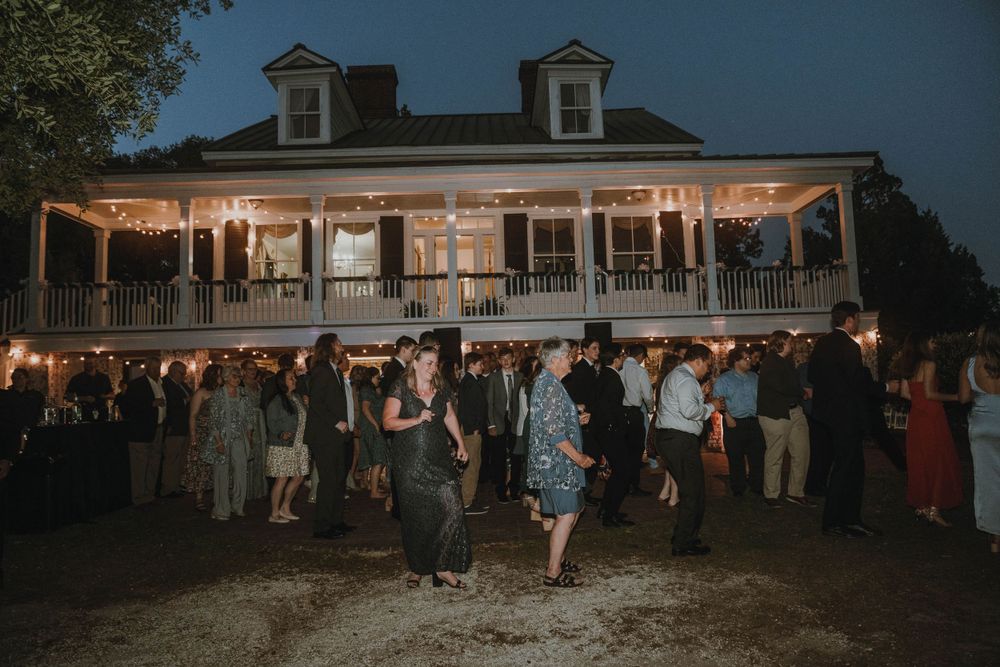 Historic southern mansion with wraparound porch lit up at night during an outdoor reception.