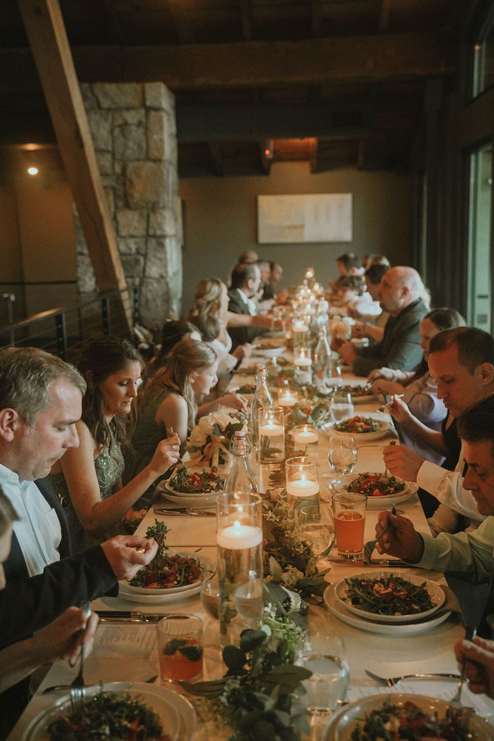 Candlelit dinner reception with guests enjoying their meals at a long banquet table.