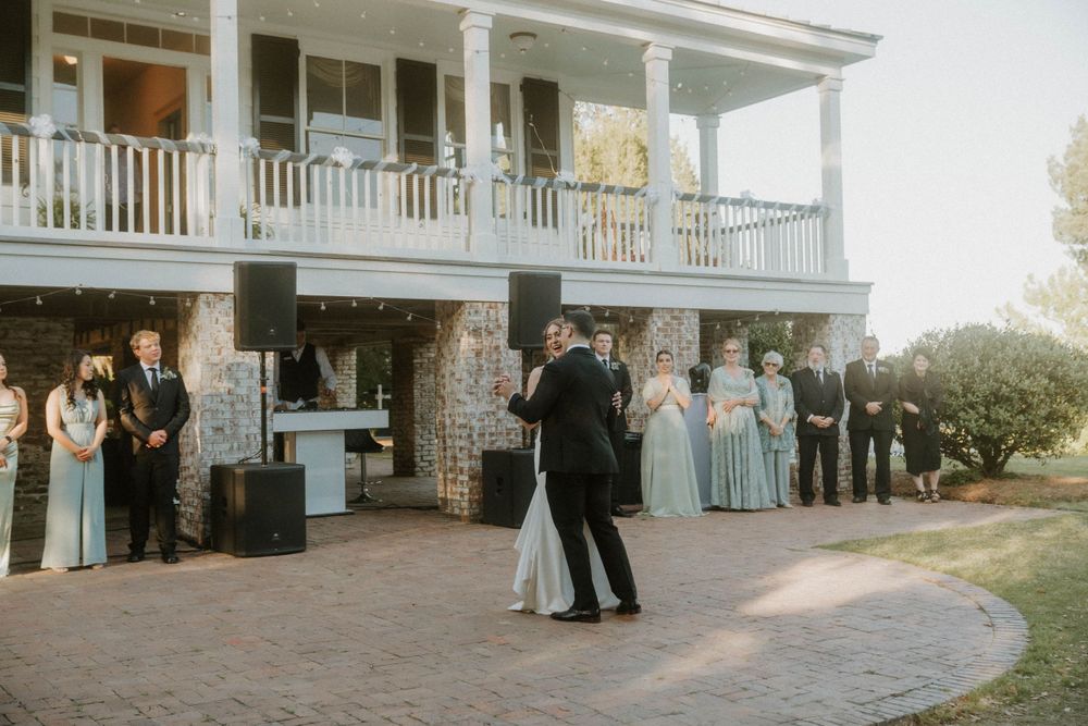 Wedding party watches first dance on patio in front of southern plantation house.