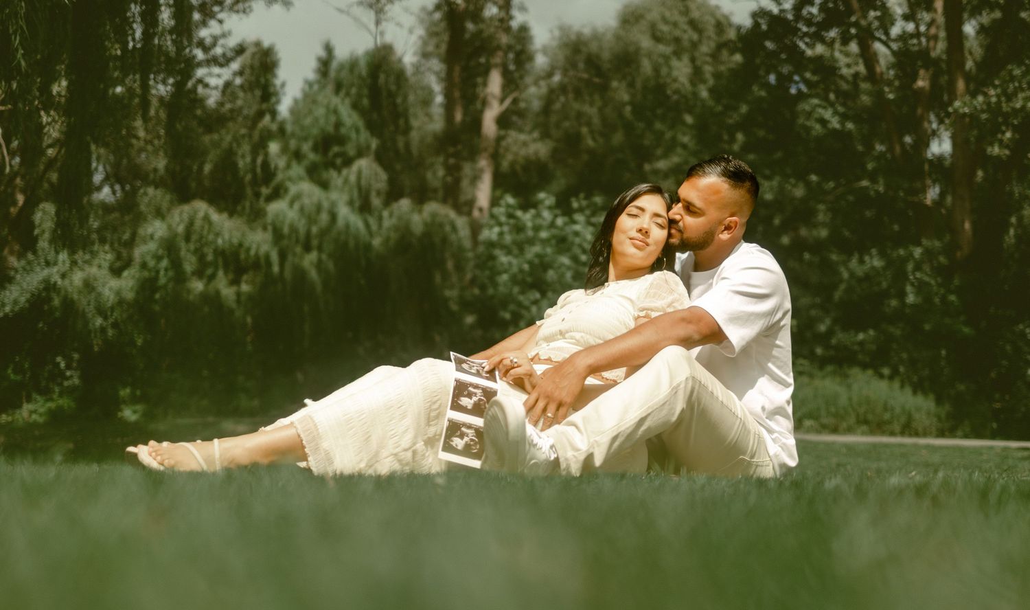 Romantic wedding couple embraces on a grassy hillside during golden hour.
