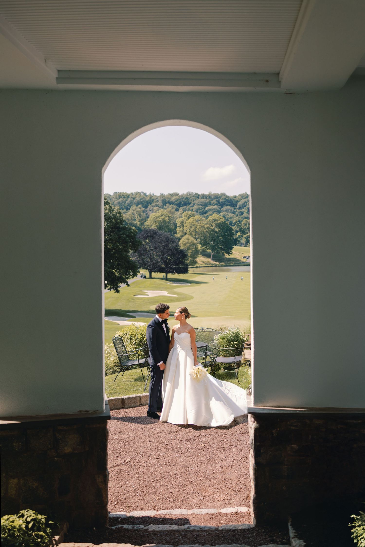 Bride and groom share a romantic moment framed by a white arched doorway overlooking a golf course.