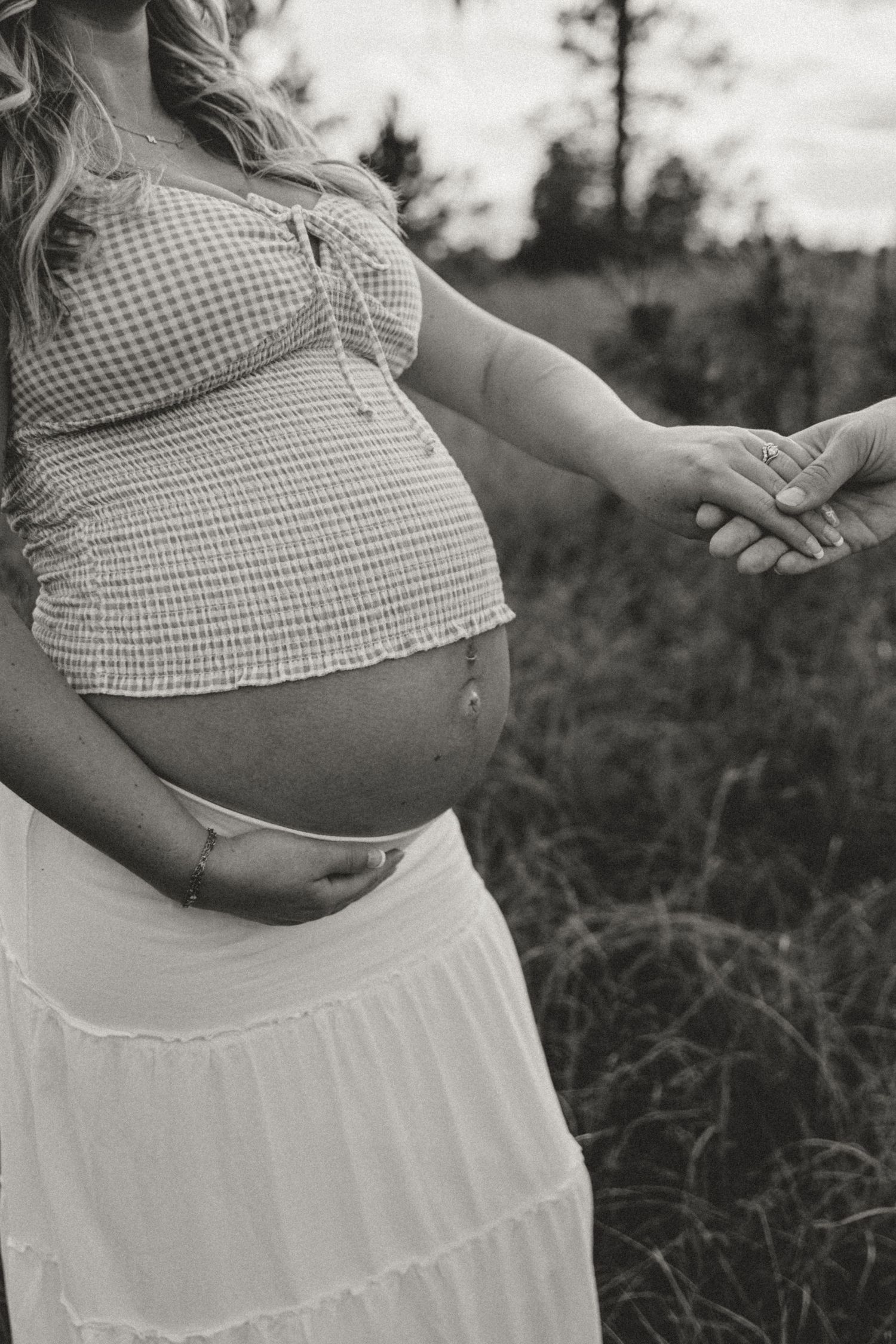 Black and white maternity photo series showcasing a growing baby bump in gingham top and flowing skirt.