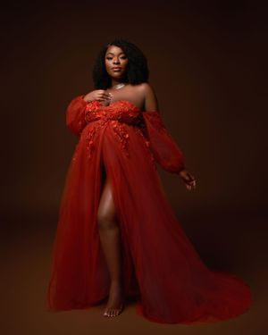 Maternity portrait in flowing red tulle gown against dark background.
