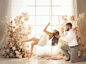 Romantic couple photo with floral arrangements and window light in soft pink tones for a maternity photo session