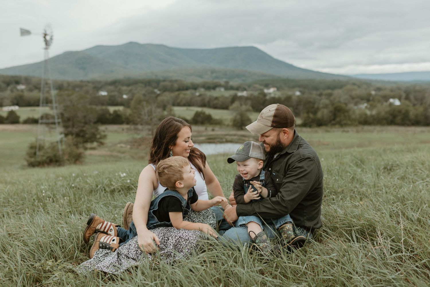 A couple shares intimate moments in a grassy field with mountains in the background.