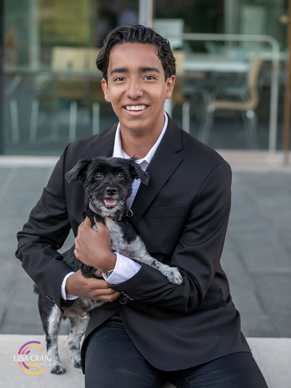 Professional in dark suit holding small grey and white dog in outdoor business setting. Senior Portrait Photographer | Denver, Broomfield,